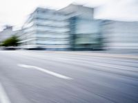 blurred picture of a street with cars driving past buildings in the background and an empty street
