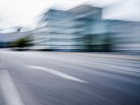blurred picture of a street with cars driving past buildings in the background and an empty street
