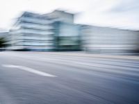 blurred picture of a street with cars driving past buildings in the background and an empty street