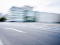 blurred picture of a street with cars driving past buildings in the background and an empty street