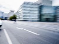 blurred picture of a street with cars driving past buildings in the background and an empty street