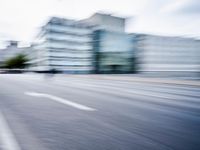 blurred picture of a street with cars driving past buildings in the background and an empty street