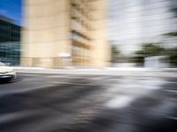 blurry view of a urban street with buildings in the background by a puddle of water