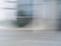 a blurry view of a modern city building in motion on a sunny day with only a red fire hydrant in front