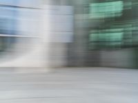 a blurry view of a modern city building in motion on a sunny day with only a red fire hydrant in front