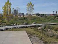 an empty parking lot is next to the boardwalk with rocks, shrubs and bushes in front of a city skyline