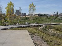 an empty parking lot is next to the boardwalk with rocks, shrubs and bushes in front of a city skyline