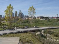 an empty parking lot is next to the boardwalk with rocks, shrubs and bushes in front of a city skyline