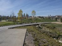 an empty parking lot is next to the boardwalk with rocks, shrubs and bushes in front of a city skyline