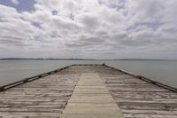 a boardwalk extending out over a wide lake with mountains in the distance and a cloudy sky