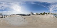 this is a fisheye lens photo of the boardwalk near the marina area, and some boats are parked on the docks