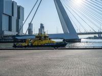 a yellow and white boat in the water next to buildings on a bridge with a few people around it