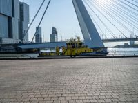 a yellow and white boat in the water next to buildings on a bridge with a few people around it