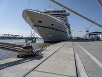 a white boat docked at the dock with some ropes on it's side and another ship in the background