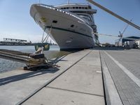 a white boat docked at the dock with some ropes on it's side and another ship in the background