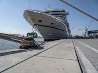 a white boat docked at the dock with some ropes on it's side and another ship in the background