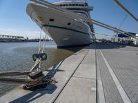 a white boat docked at the dock with some ropes on it's side and another ship in the background