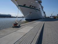 a white boat docked at the dock with some ropes on it's side and another ship in the background