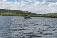 the boat is floating near a large forested hill of trees in the lake and on a cloudy day