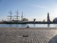 a small boat sitting on top of a brick ground near a river with ships in the background