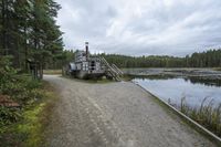 a boat with a ramp sitting in the gravel next to water in the woods while cloudy sky above