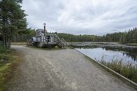 a boat with a ramp sitting in the gravel next to water in the woods while cloudy sky above