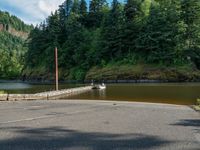 a boat sits on the water at the footbridge in a forest area near a road and a river