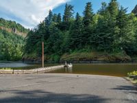 a boat sits on the water at the footbridge in a forest area near a road and a river