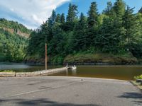 a boat sits on the water at the footbridge in a forest area near a road and a river