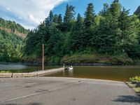 a boat sits on the water at the footbridge in a forest area near a road and a river