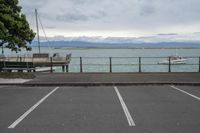 several boats are in a bay on the water with mountains behind them, some sit in a parking lot near a wooden fence