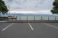 several boats are in a bay on the water with mountains behind them, some sit in a parking lot near a wooden fence