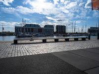 several benches are sitting near the water with boats in the distance on a brick path