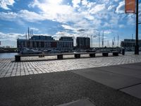 several benches are sitting near the water with boats in the distance on a brick path