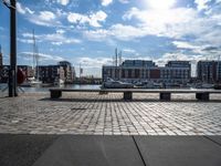 several benches are sitting near the water with boats in the distance on a brick path