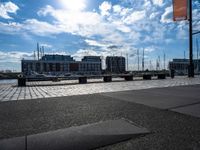 several benches are sitting near the water with boats in the distance on a brick path