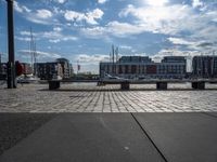 several benches are sitting near the water with boats in the distance on a brick path