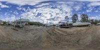 a 360 camera view looking up at some boats on dirt and water with a few trees in the background