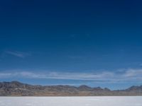 an image of snowboarders out on a flat surface in the desert near mountains