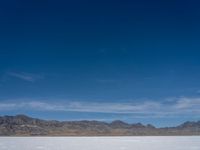 an image of snowboarders out on a flat surface in the desert near mountains