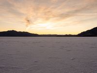 a small dog walking across a salt field at sunset next to the sun light and mountains