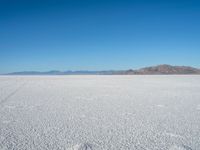 a barren plain with lots of snow and rocks, with a clear blue sky in the background