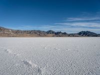 a wide open desert area with mountains and snow covered ground around it, in a blue sky