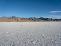 a wide open desert area with mountains and snow covered ground around it, in a blue sky