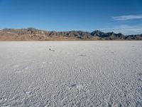 a wide open desert area with mountains and snow covered ground around it, in a blue sky