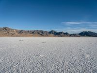 a wide open desert area with mountains and snow covered ground around it, in a blue sky