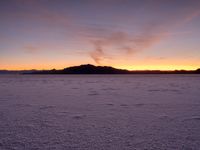 a person walking across a large field at sunset with their umbrella on the snow covered ground