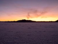 a person walking across a large field at sunset with their umbrella on the snow covered ground