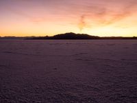 a person walking across a large field at sunset with their umbrella on the snow covered ground