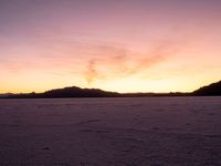 a person walking across a large field at sunset with their umbrella on the snow covered ground